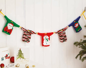 A Christmas garland - yellow rope with mini Christmas jumpers spaced along it. You can see a green sweater with a Santa motif, a red one with a snowman and teal with elf. The other two are knitted in green, white and red self-striping glitz yarn