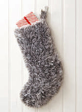 Load image into Gallery viewer, Image of a large Christmas stocking hand knitted in grey or silver coloured faux fur yarn. Pictured hanging on a red door with a wrapped present sticking out the top
