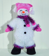 Load image into Gallery viewer, White tinsel snowman with pink tinsel cuffs and boot tops. Black boots in DK yarn. Head, carrot nose and pink hands also knitted in DK yarn. Pink hat has white Fair Isle effect detail with a white tassel on each corner. Tinsel scarf with pink pompoms