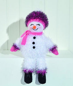 White tinsel snowman with pink tinsel cuffs and boot tops. Black boots knitted in black DK yarn. The head, carrot nose and pink hands are also knitted in DK yarn. Pink seed stitch scarf and pink tinsel bobble hat with pink band and white pompom