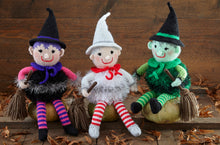 Load image into Gallery viewer, 3 hand-knitted witches sitting on wooden pumpkins. They all have a hat, neck tie, tinsel body and striped stockings and are holding a broomstick. One is black with pink arms, one is white and silver with red and white stockings and the other is green