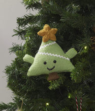 Load image into Gallery viewer, Fun Christmas tree ornament. Hand knitted in light green yarn using stocking stitch. It is a triangle shape with green arms and a brown trunk. A mouth and eyes have been added with a gold coloured star at the top
