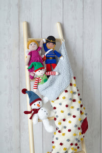 Close up of the top of the stocking showing the cotton wool textured band, cream stocking stitch and red, silver and yellow bobbles. A snowman toy sits with this pompom hat and scarf, a green elf, pink fairy and drummer boy toy are all shown