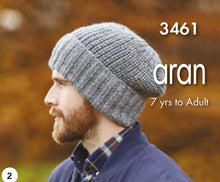 Load image into Gallery viewer, Image of a man wearing a rib beanie hat with rib turn back. The main section of the hat is knitted using Fisherman's rib stitch for a chunky rib finish. The hat is hand knitted in a light to mid grey Aran yarn