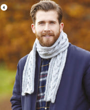 Load image into Gallery viewer, Image of a man wearing a hand knitted scarf knitted in a light grey Aran yarn. The centre of the scarf features a V effect cable design