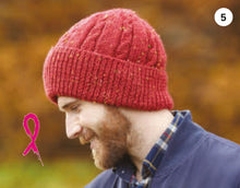 Load image into Gallery viewer, Image of a man wearing a snug fitting beanie hat. The hat is hand knitted in a red Aran yarn with light flecks. The hat features a deep rib turn back and the main section alternates broad stocking stitch panels with cable twists