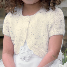 Load image into Gallery viewer, Close up image of young girl wearing a white dress and cream round neck bolero cardigan or shrug. The bolero has short sleeves and the yarn is interwoven with silver sequins to make it sparkle
