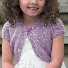 Load image into Gallery viewer, Close up image of young girl wearing a white dress with a dusky purple round neck bolero cardigan or shrug. The bolero has capped sleeves and the yarn is interwoven with silver sequins to make it sparkle
