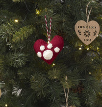 Load image into Gallery viewer, A dark red love heart knitted Christmas tree ornament shown hanging on a tree. The heart has a white paw print added to the front and the hanging loop is a twist of red and white yarn