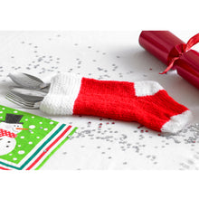 Load image into Gallery viewer, Hand knitted cutlery stocking. Knitted in stocking stitch with a garter stitch top band. The band, toe and heel are knitted in white DK yarn and the main section in red. Shown on a festive table with cutlery but it can also be used as a mini gift bag