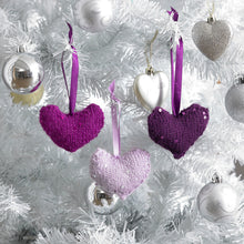 Load image into Gallery viewer, Three hand knitted heart shaped Christmas decorations. Shown in purple, cerise and lilac they are trimmed with sequins and a length of hanging ribbon.