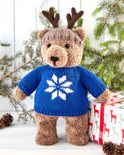 Load image into Gallery viewer, Hand knitted furry teddy bear in a traditional design. He has a light brown beanie hat with dark brown antlers to dress him up like a reindeer. He wears a royal blue Xmas sweater with white snowflake motif on the front
