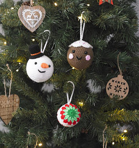 3 Christmas tree baubles hanging on a tree with white hanging loops. 1 is a brown pudding with white top, black face features and pink cheeks. The snowman has a black hat and orange carrot nose. One has a green then light green, red and white rounds