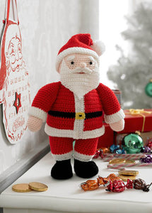 Crocheted Santa or Father Christmas toy. He stands on his black boots and wears traditional Santa Claus clothes - white trimmed red trousers, jacket and hat with a white pom pom. His black belt has a gold buckle and he has a white beard and moustache