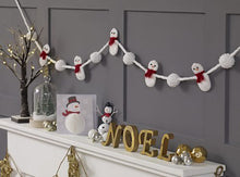 Load image into Gallery viewer, Simple but fun and effective crocheted snowman garland. The hanging cord is white and the snowmen are attached as if the cord is their arms. They are alternated with which pompoms. The snowmen wear red scarves and have black eyes and an orange nose