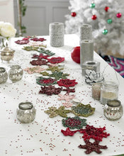 Load image into Gallery viewer, A stunning festive table runner or table centre decoration. A variety of designs and sizes of snowflakes and stars are sewn together at the tips to give an irregular long, thin shape. The yarns are reds, greens, browns and pinks with sparkle threads 
