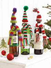 Load image into Gallery viewer, 3 wine bottles sitting on drawers. Each bottle has a different coloured scarf with matching bobble hat. Green, purple and red stripes; red, white and a sparkle mix; red, green and white. The scarf has tassels and the hat is topped with a mini pom pom
