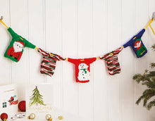 Load image into Gallery viewer, A Christmas garland - yellow rope with mini Christmas jumpers spaced along it. You can see a green sweater with a Santa motif, a red one with a snowman and teal with elf. The other two are knitted in green, white and red self-striping glitz yarn
