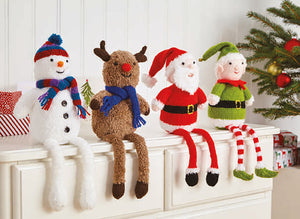 4 hand knitted shelf sitters on top of drawers. All have long legs dangling over the edge. The snowman has a stripy scarf and pom pom hat, rudolph is wearing a blue scarf, Father Christmas and an elf with red and white striped legs finish the group