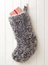Load image into Gallery viewer, Image of a large Christmas stocking hand knitted in grey or silver coloured faux fur yarn. Pictured hanging on a red door with a wrapped present sticking out the top

