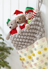 Load image into Gallery viewer, Close up of a large crocheted Xmas stocking. The main section is cream with pale pink, silver, gold and grey bobbles. The top is silver bobbles. Sticking out the top are 3 crocheted toys - a bear with a bow on its head, bear with Santa hat and an Elf
