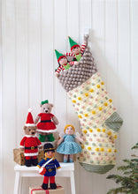 Load image into Gallery viewer, Image of crocheted Christmas stocking and toys. Two elves are sticking out of the spotted festive stocking and, arranged on a stool to the side, are Father and Mother Christmas bear toys, a drummer boy and fairy in a blue dress
