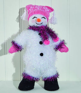 White tinsel snowman with pink tinsel cuffs and boot tops. Black boots in DK yarn. Head, carrot nose and pink hands also knitted in DK yarn. Pink hat has white Fair Isle effect detail with a white tassel on each corner. Tinsel scarf with pink pompoms