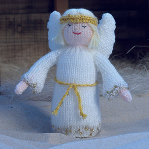 The angel from the nativity scene. Hand knitted in cream DK yarn with gold sparkle trim along the bottom and cuffs of her gown. A gold head dress and wings complete the look with a gold tie around her waist