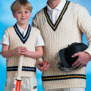 Close up image of boy wearing traditional cricket vest and holding a cricket bat standing next to a man in a traditional v neck cricket jumper holding a hat and cricket ball