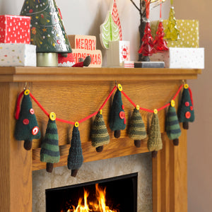 Festive mantlepiece with Christmas tree knitted bunting. Trees are attached to a red knitted cord with yellow buttons. There are 4 Xmas tree designs - dark green with red buttons, dark and light green stripes, dark and olive green stripes, dark green