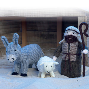 Shepherd, sheep and donkey from the nativity scene. The donkey is knitted in grey yarn with a lighter muzzle and black feet. The sheep is cream with a textured coat. The shepherd wears a dark brown robe with beige head dress, beard and holds a staff
