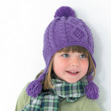 Load image into Gallery viewer, Image of young girl wearing a hand knitted Aran hat in purple yarn. The hat is a pom pom or bobble helmet style hat with ear flaps and tassels. The main section is knitted in moss or seed stitch with cable twist and a diamond cable panel at the front
