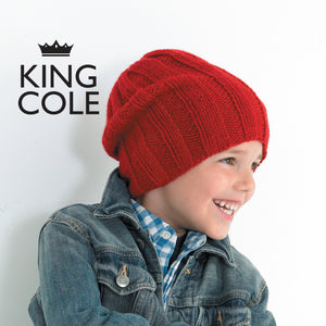 Image of young boy smiling and wearing a red hand knitted Aran hat in red yarn. The hat is a slouchy beanie with broad rib