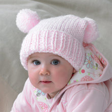 Load image into Gallery viewer, This baby is wearing a super cute pink tea bag hat in chunky baby yarn. Hand knitted with a rib turn back and stocking stitch main section. The main hat is a square shape and finished with a pom pom on each corner. The weight folds it over 
