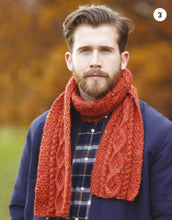 Load image into Gallery viewer, Image of a man wearing a hand knitted scarf knitted in a red Aran yarn with yellow and lighter flecks. The centre of the scarf features a diamond cable design with a cable twist along either side. The edge panels are knitted using moss or seed stitch
