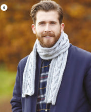 Load image into Gallery viewer, Image of a man wearing a hand knitted scarf knitted in a light grey Aran yarn. The centre of the scarf features a V effect cable design
