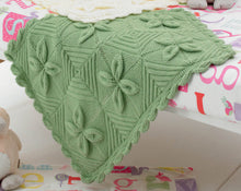 Load image into Gallery viewer, Close up of green pram baby blanket in green yarn. Knitted in squares with four leaf motifs meeting at a corner. The rest of the square is knitted in a diagonal - half garter stitch and half stocking and garter stitch. Finished with a leaf border
