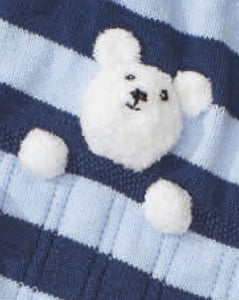 Cropped image of a white teddy bear head and front paws knitted in fake fur yarn. The bear is sewn on a navy and light blue striped baby blanket so that the bear looks like it is asleep in bed under the covers