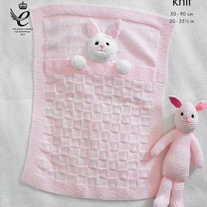 Close up of pale pink baby blanket with garter stitch border, square textured main design. The blanket has the head and front paws of a rabbit attached to look like it is in bed. Garter stitch rabbit toy also shown. Knitted in DK baby yarn