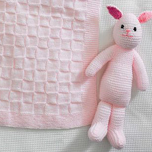 Close up of pale pink knitted rabbit toy. Hand knitted in garter stitch with pink embroidered nose and mouth and black eyes. Fronts of ears are a bright pink. You can also see the square texture of the baby blanket