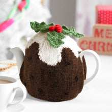 Load image into Gallery viewer, Fun tea cosy Christmas pudding. Knitted in dark brown yarn with black spots. The white yarn at the top is knitted in an irregular shape to look like poured cream. The pudding is topped with 3 green holly leaves and red berries.
