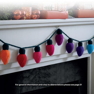 A garland of knitted fairy lights hanging on a mantlepiece. The string and tops of each light are knitted in bottle green DK yarn. Each light is a different colour from orange to shades of pink and red, purples and blue