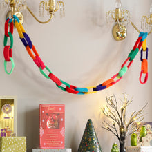 Load image into Gallery viewer, A retro, fun and colourful Christmas garland knitted in the style of a paper chain. Hanging between two wall lights. This is a fun, easy to knit and very effective twist on an Xmas garland or bunting
