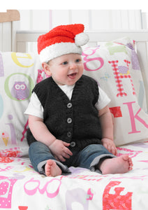Baby sitting on a bed and wearing a hand knitted Santa hat. The yarn has a furry texture and the main section is knitted in red with a white brim and matching white pom pom 