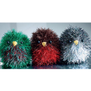Three Xmas birds knitted in tinsel yarn. The left hand one is emerald green with a mix of red and green breast. In the middle is a traditional brown robin with red breast. To the right is a black mixed with coloured strands and white breast