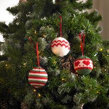 Load image into Gallery viewer, 3 Christmas tree bauble ornaments on a tree. 1 is knitted in festive red, green and white stripes. 1 is white with two rows of red zig zags around the middle. 1 is green top and bottom with a white centre band with red hearts and edged with red
