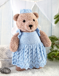 Light brown traditional teddy knitted in fake fur yarn. The bear wears a Christmas fairy outfit in pale blue. The dress has ruffle capped sleeves and the skirt of the dress is knitted in cable and lace stitches. White wings and a light blue crown 