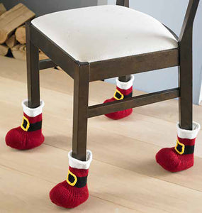 Photo of a dining chair with a Santa boot at the bottom of each leg. The boots are knitted in dark red stocking stitch with white tops and a black belt with gold buckle