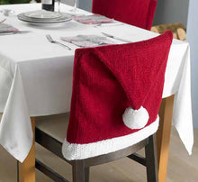 Load image into Gallery viewer, Photo of a Christmas chair cover. The main hat piece is knitted in stocking stitch using a dark red yarn. The white band is knitted knitted in moss or seed stitch for texture. The top of the hat is folded over the chair back with a white pompom

