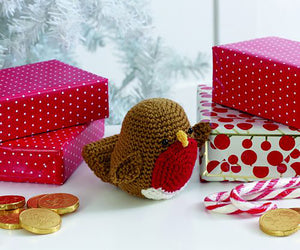 Crocheted festive robin toy. The main bird is crocheted in brown with matching wings and tail pieces. The eyes are beads and the beak is gold. On the front is a crocheted circle in red for its breast with a white strip around the bottom